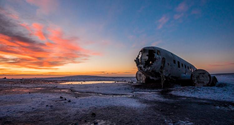 Een neergestort vliegtuig in een woestijnlandschap tijdens zonsondergang.