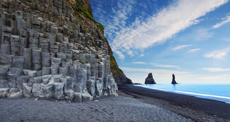 Een zicht op een zwart zandstrand met basaltzuilen en zeerotsen.