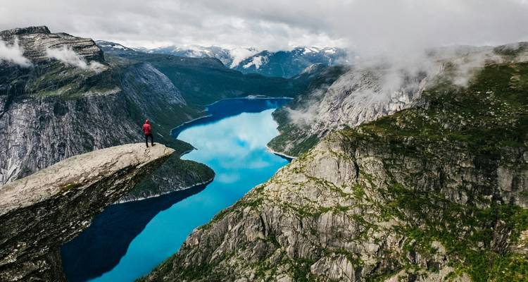Person standing at the edge of a cliff overlooking a fjord.