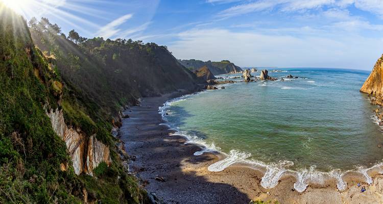 A secluded beach with cliffs and turquoise water under sunbeams.