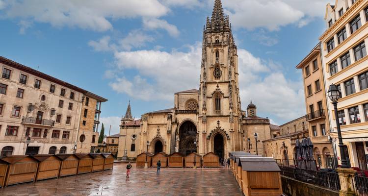 Cathedral façade and plaza with people walking, against a cloudy sky.