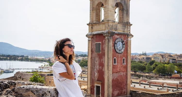 Femme debout près d'un clocher historique avec une vue panoramique sur la ville.