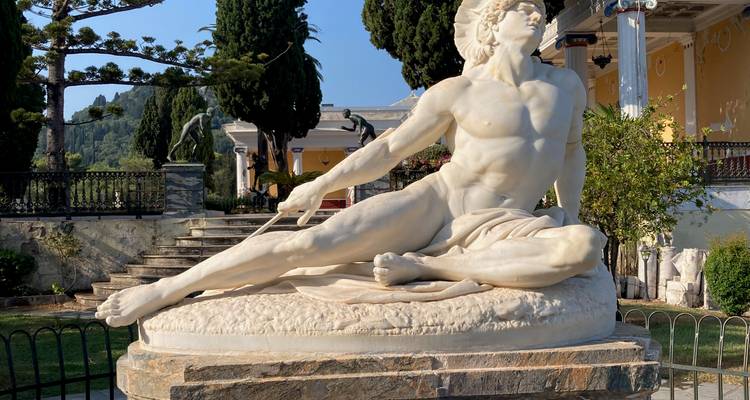Statue de marbre blanc d'une figure allongée dans un jardin.