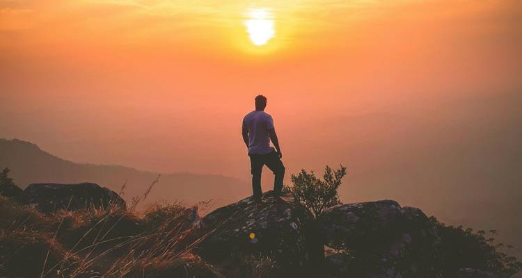 Silhouette d'une personne debout sur des rochers avec un coucher de soleil en arrière-plan.