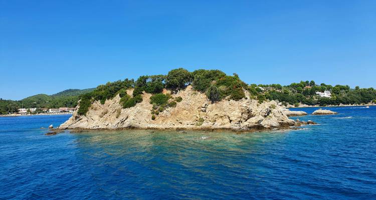 Small rocky island surrounded by clear blue sea.