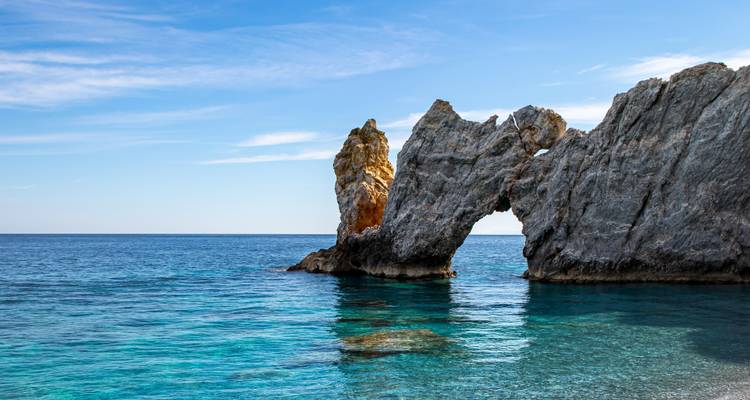 Rocky arch over clear blue water against a clear sky.