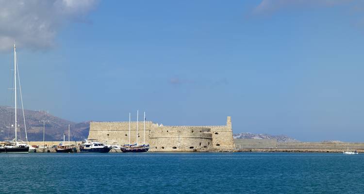 Fortress wall by the sea with yachts docked nearby.