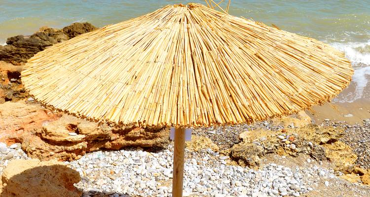 Close-up of a straw beach umbrella on a rocky shore.