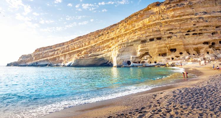Seaside rocky cliffs with caves and people on a beach.