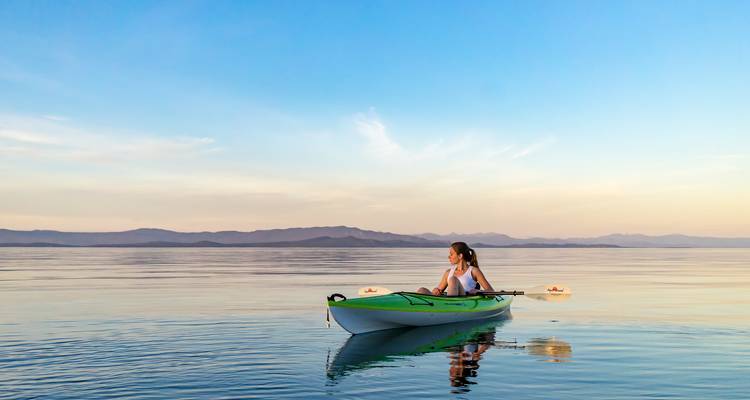 Mujer navegando en kayak en un mar tranquilo durante el atardecer.