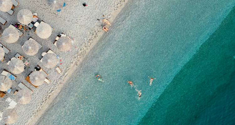 Playa con tumbonas y personas nadando desde arriba.