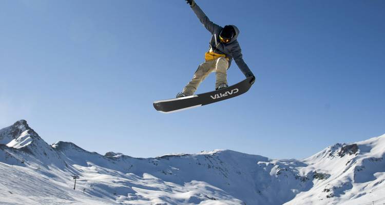 Snowboarder performing a jump with snowy mountains in the background.