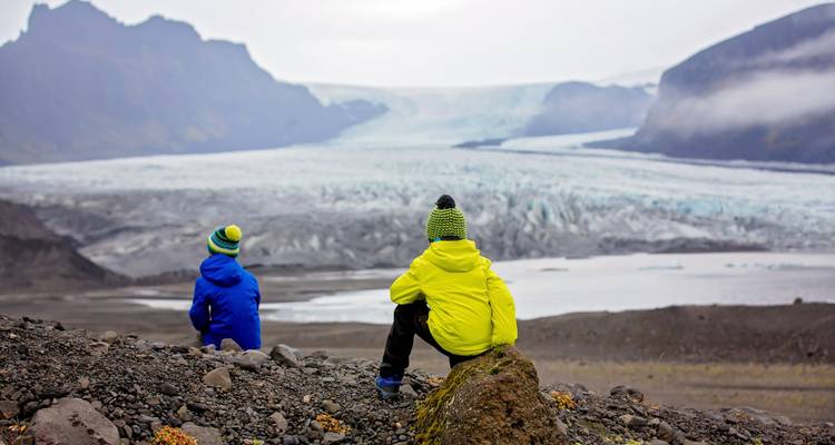 Children sitting on rocks admiring a glacier.