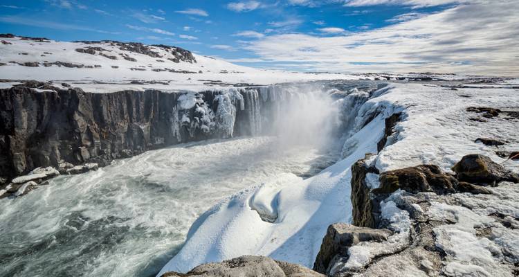 Wide view of a powerful waterfall over icy rocks.