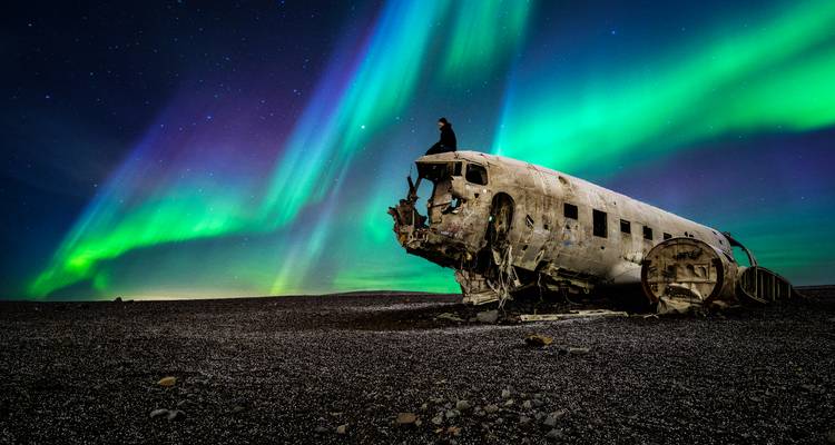 Northern lights over a crashed airplane with a person on it.