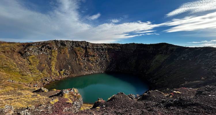 Crater lake surrounded by rocky cliffs under blue sky.
