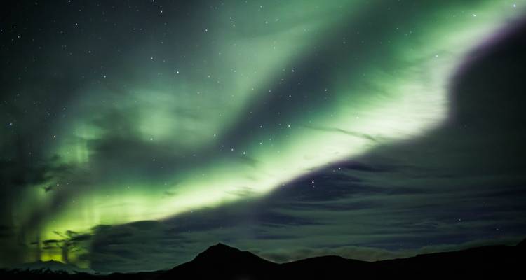 Northern Lights in a starry night sky over mountains.