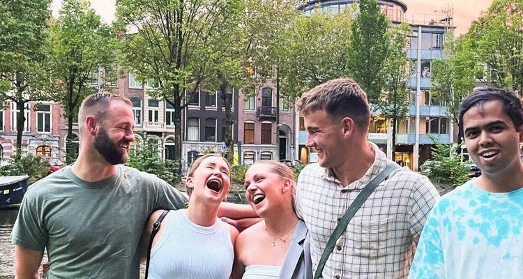 Cinq jeunes amis qui rient ensemble au bord d'un canal bordé d'arbres avec d'étroites maisons hollandaises en arrière-plan