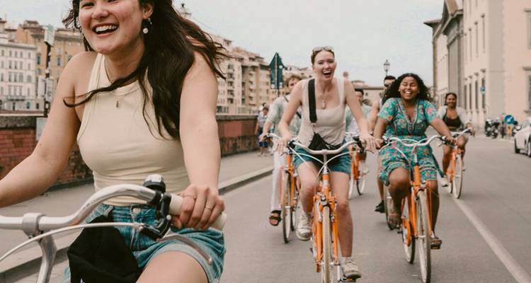 Groep reizigers die genieten van een stadsfietsrit op bijpassende oranje fietsen, lachend terwijl ze trappen.
