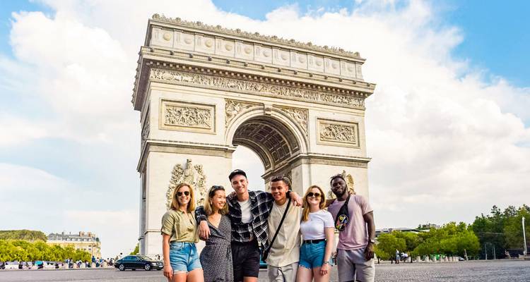 Six voyageurs souriants posent devant l'Arc de Triomphe par une journée ensoleillée.