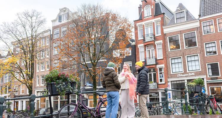 Three people chatting on a bridge with bicycles and historic buildings around.