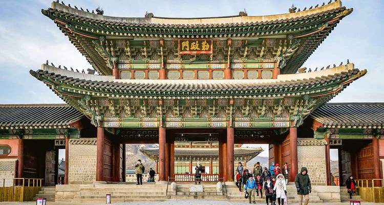 Porte de palais coréen traditionnel avec des visiteurs qui entrent.