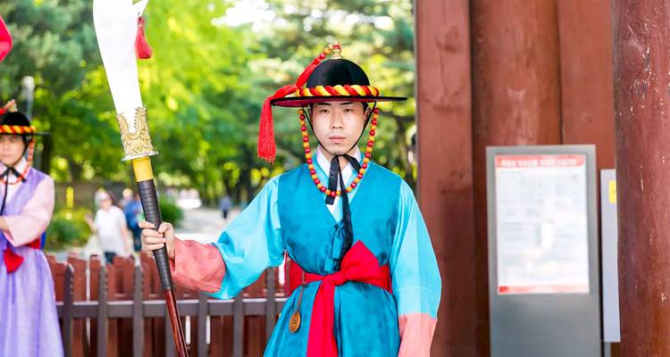 Garde coréen traditionnel en tenue de cérémonie tenant un bâton sur un site historique.
