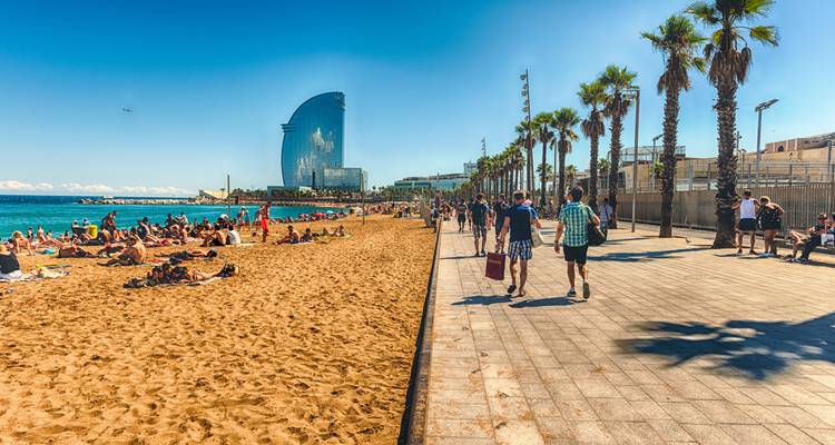 Plage avec des gens qui marchent et le bâtiment W Barcelona en vue.