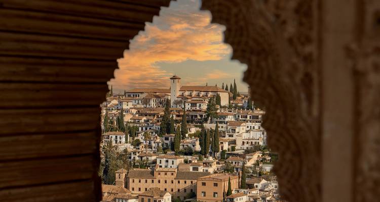 Alhambra-Blick gerahmt von einem verzierten Bogen bei Sonnenuntergang.