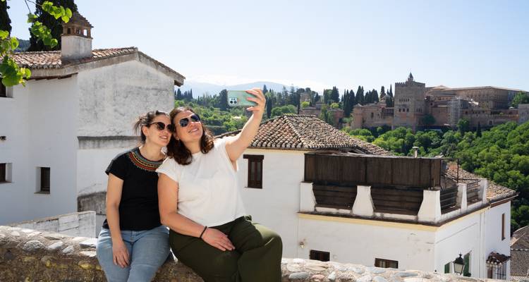 Zwei Frauen machen ein Selfie mit der Alhambra im Hintergrund.