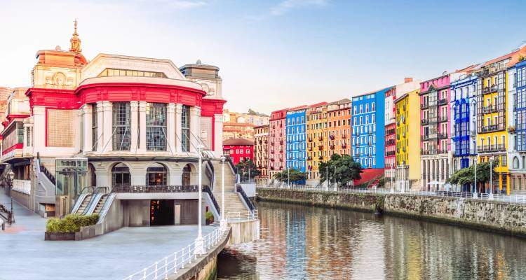 Bunte Gebäude entlang eines Flusses mit einem ikonischen Bilbao-Markt.
