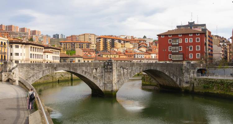 Steinbogenbrücke über einem Fluss mit traditionellen Gebäuden in Bilbao.