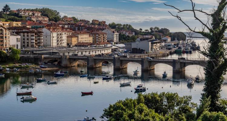 Küstenstadtansicht mit einer Brücke und Booten auf ruhigem Wasser.
