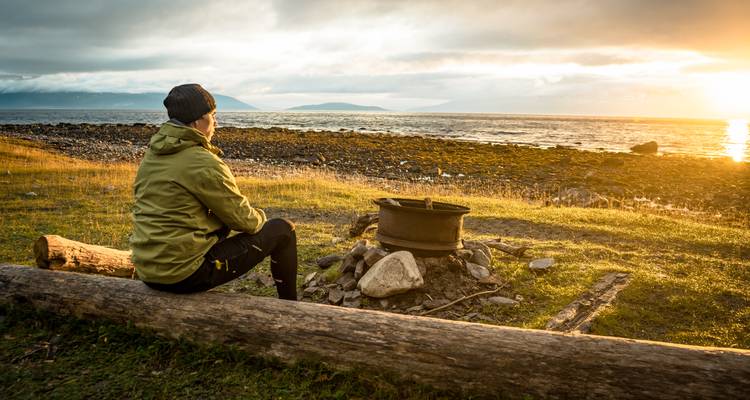 Personne assise près du foyer regardant le coucher de soleil sur l'océan.
