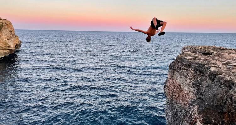 Person performing a backflip into the sea during sunset.