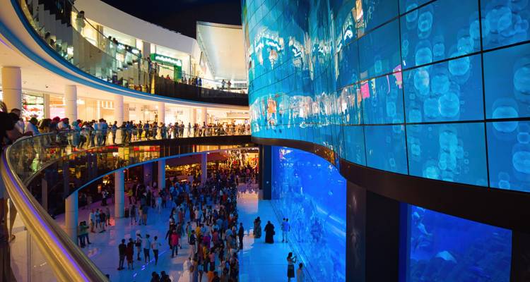 Centre commercial intérieur animé avec grand aquarium et foules.