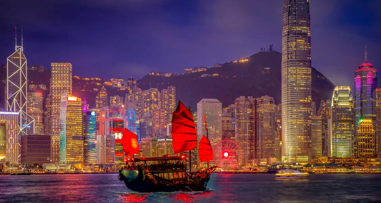 Traditional junk boat in front of a brightly lit city skyline at night.