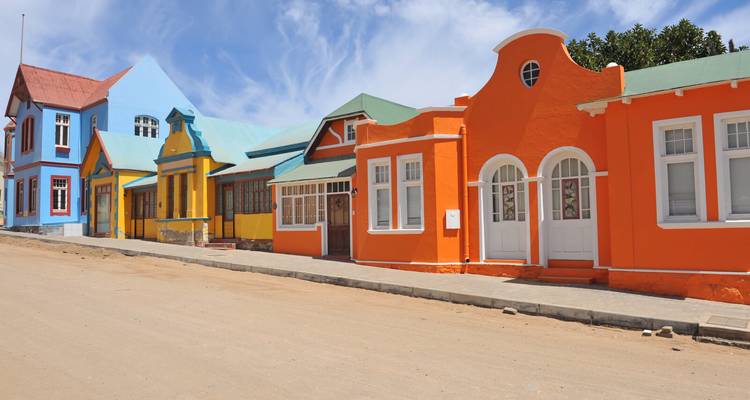 Maisons colorées de style colonial le long d'une rue sablonneuse.
