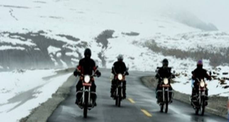 Four motorcyclists riding on a snowy mountain road.