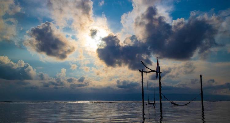 Serene ocean view at sunset with hammock over the water.