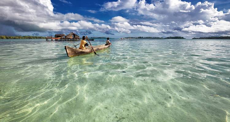 Two people paddling a wooden canoe in clear shallow waters.