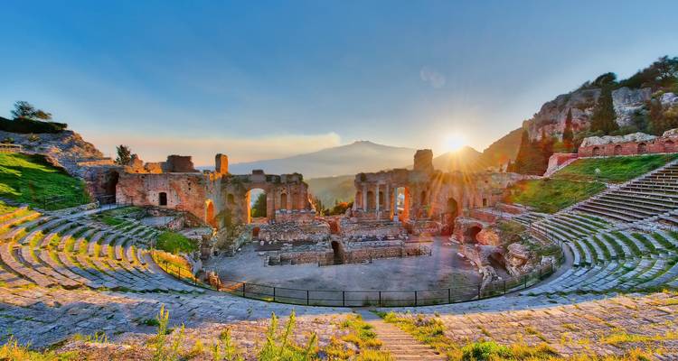 Ruines d'amphithéâtre antique avec une montagne en arrière-plan.