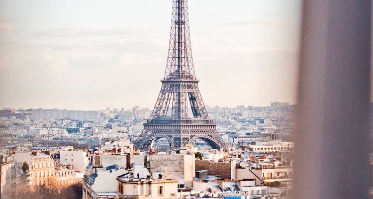 The Eiffel Tower rises above the Paris skyline in soft dawn light, framed by city rooftops.
