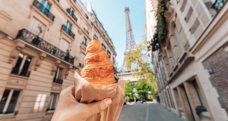 Hand die een croissant vasthoudt met de Eiffeltoren op de achtergrond.