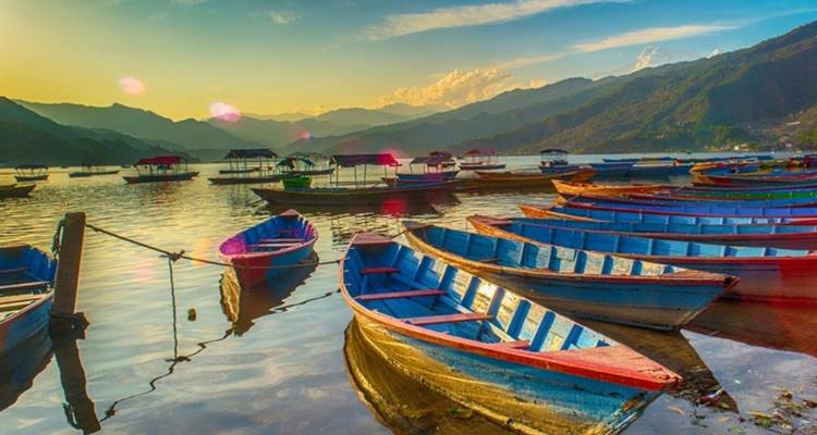 Botes coloridos en un lago con un telón de fondo montañoso durante el atardecer.