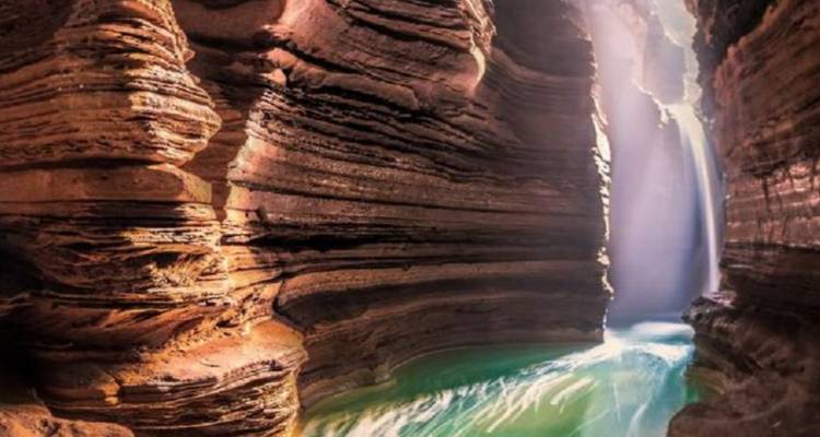 Una cascada que fluye a través de un desfiladero estrecho con luz solar brillando a través.