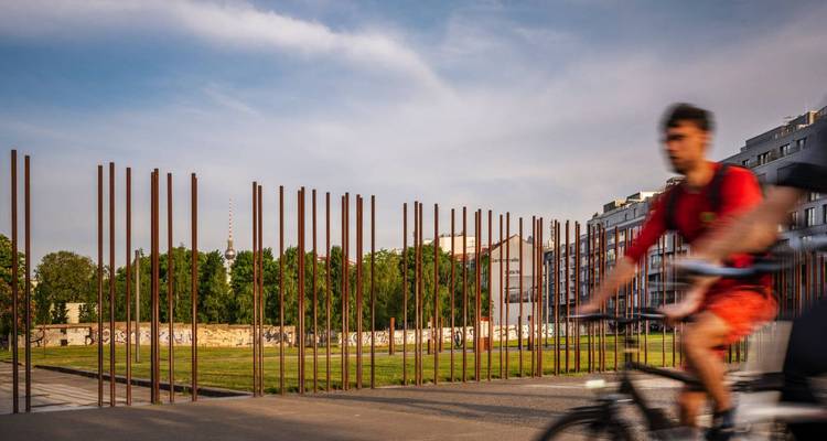 Cycliste flou passant devant une installation de poteaux métalliques.