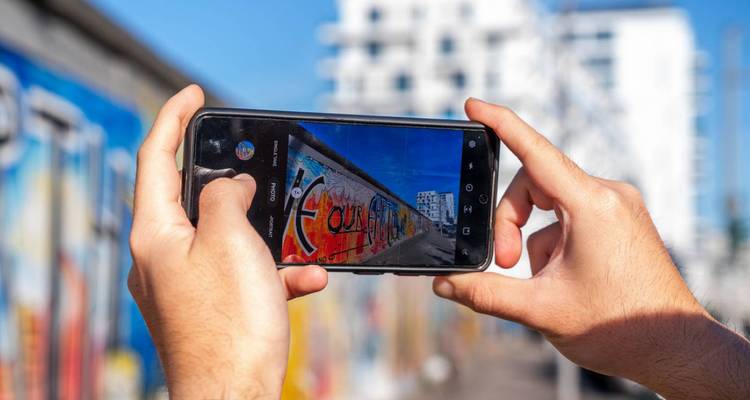 Mains tenant un smartphone prenant des photos d'une fresque murale.