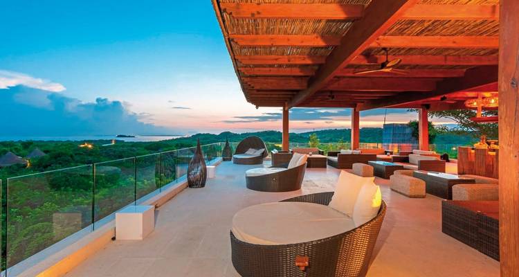 Terrasse sur le toit avec sièges et vues sur une zone côtière au coucher du soleil.