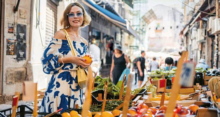 Marktscène met een vrouw die fruit aan het kopen is.